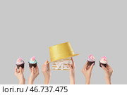 Множество женских рук с праздничными капкейками, праздничной шляпой и подарочной коробкой на сером фоне. Стоковое фото, фотограф Pixel_shot / Фотобанк Лори