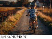 A cheerful little boy rides a bicycle in a helmet outdoors. A happy child is engaged in an active sport. Protection. Life insurance and child safety. Стоковое AI-изображение, AI-художник Photojuli / Фотобанк Лори