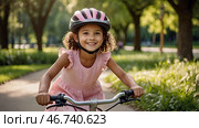 A cheerful girl in a pink dress rides a bicycle in a helmet in the park. A happy child is engaged in an active sport. Protection. Life insurance and child safety. Стоковое AI-изображение, AI-художник Photojuli / Фотобанк Лори