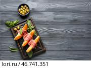 Вкусный дынный с пршутто, базиликом и зелеными оливками на темном деревянном фоне. Стоковое фото, фотограф Pixel_shot / Фотобанк Лори