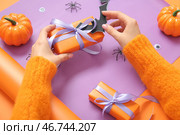 Женщина с украшениями заворачивает подарочные коробки для Хэллоуина на фиолетовом фоне. Стоковое фото, фотограф Pixel_shot / Фотобанк Лори