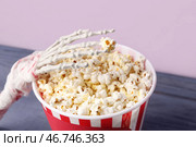 Ведро с попкорном с изображением костяной руки Хэллоуина на деревянном столе на заднем плане лайлакового цвета, крупным планом. Стоковое фото, фотограф Pixel_shot / Фотобанк Лори