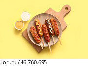 Тарелка с вкусными корн-догами и миски с соусами на желтом фоне. Стоковое фото, фотограф Pixel_shot / Фотобанк Лори