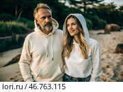 A handsome young woman and a man in white hooded sweatshirts on the beach. Template layout for hoodie design, print area layout for logo or design. Стоковое AI-изображение, AI-художник Photojuli / Фотобанк Лори
