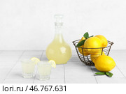 Стопки вкусного лимончелло и корзина с лимонами на светлом фоне. Стоковое фото, фотограф Pixel_shot / Фотобанк Лори