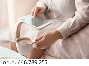 Молодая женщина, использующая планшетный компьютер и пьющая кофе дома. Стоковое фото, фотограф Pixel_shot / Фотобанк Лори
