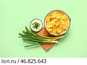 Миска вкусной сметаны с нарезанным луком-пореем и картофельными чипсами на зеленом фоне. Стоковое фото, фотограф Pixel_shot / Фотобанк Лори