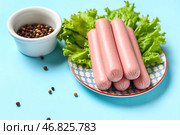 Тарелка с вкусными тонкими сосисками и салатом на голубом фоне. Стоковое фото, фотограф Pixel_shot / Фотобанк Лори