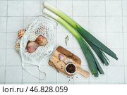 Деревянная доска и сетчатая сумка с разными видами лука на белом плиточном фоне. Стоковое фото, фотограф Pixel_shot / Фотобанк Лори