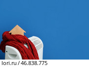 Фигура дома с теплым шарфом на электрическом конвекторном обогревателе около голубой стены дома. Концепция экономии отопления. Стоковое фото, фотограф Pixel_shot / Фотобанк Лори