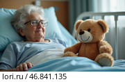 In a serene hospital room, an elderly woman relaxes in bed, softly smiling at her cuddly teddy bear. This heartwarming moment reflects warmth and comfort amidst her hardship. Стоковое AI-изображение, AI-художник Юлия Петровская / Фотобанк Лори