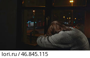 Lonely young woman looks out night window. Media. Young woman sits on window and looks sadly at night city. Woman with depression sits alone on window of house. Стоковое фото, фотограф Данил Руденко / Фотобанк Лори