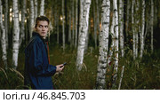 Man wanders in forest and looks around anxiously. Stock. Young man walks in woods with phone and looks around anxiously. Man is lost in woods with phone and looks around in fear. Стоковое фото, фотограф Данил Руденко / Фотобанк Лори