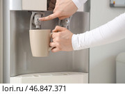 Женские руки наполняют чашку фильтрованной водой из кулера в комнате. Стоковое фото, фотограф Pixel_shot / Фотобанк Лори