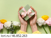 Женские руки с подарочной коробкой, красивыми цветами ранункулюса и эвкалиптом на зеленом фоне. Стоковое фото, фотограф Pixel_shot / Фотобанк Лори