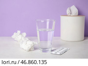 Стакан воды с таблетками и коробкой для салфеток на столе возле сиреневой стены. Концепция аллергии. Стоковое фото, фотограф Pixel_shot / Фотобанк Лори