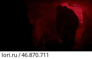 red signal flare burning inside dark natural cave making shadows on cave walls. Стоковое фото, фотограф David Kashakhi / Фотобанк Лори