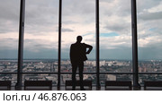 Rear view of man in formal suites who stand in front of panoramic window with city view. Стоковое фото, фотограф David Kashakhi / Фотобанк Лори
