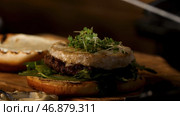 Close up of male hands putting green microgreen of mustard on camembert cheese of homemade hamburger with sauce, foodporn concept. Стоковое фото, фотограф David Kashakhi / Фотобанк Лори