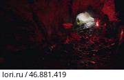 Man moving inside the dark and mysterious cavern with a red burning signal flare in his hand. Стоковое фото, фотограф David Kashakhi / Фотобанк Лори