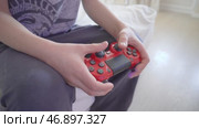Игровой процесс с красным геймпадом PlayStation вид сбоку. Ребёнок играет в видеоигру, держа в руках красный геймпад PlayStation. Редакционное видео, видеограф Анна Чижова / Фотобанк Лори