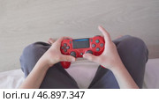 Игровой процесс с красным геймпадом PlayStation вид сбоку. Ребёнок играет в видеоигру, держа в руках красный геймпад PlayStation. Редакционное видео, видеограф Анна Чижова / Фотобанк Лори