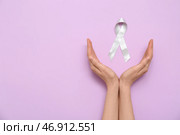 Женские руки с серой ленточкой осведомленности на фиолетовом фоне. Концепция рака мозга. Стоковое фото, фотограф Pixel_shot / Фотобанк Лори