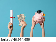 Женские руки держат диплом, деньги и копилку в форме свиньи с декоративной шапочкой выпускника на синем фоне. Стоковое фото, фотограф Pixel_shot / Фотобанк Лори