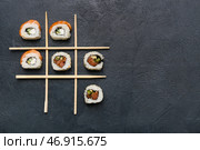 Игра в крестики-нолики с вкусными суши-роллами и палочками на черном фоне с текстурой. Стоковое фото, фотограф Pixel_shot / Фотобанк Лори