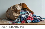 Clothes spill out of a large paper bag on a wooden surface during a decluttering project in a bright room. Стоковое AI-изображение, AI-художник Сергей Толмачёв / Фотобанк Лори