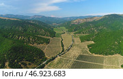 Beautiful view from above of farm fields surrounded by high mountains covered with green trees and shrubs in summer sunny day against blue sky. Стоковое фото, фотограф David Kashakhi / Фотобанк Лори