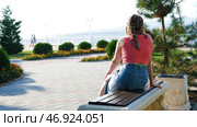 Woman is sitting alone on bench among well-groomed flower beds of park on background of vacationing people on sunny day. Стоковое фото, фотограф David Kashakhi / Фотобанк Лори