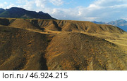Close-up view of sand and gravel hills and ravines near the mountains covered with green shrubs and trees against blue sky. Стоковое фото, фотограф David Kashakhi / Фотобанк Лори