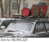 Кладовка ненужных вещей на крыше старой автомашины марки "Волга". К багажнику крепко привязаны цепями и веревками  припорошенные снегом старые ненужные вещи: лыжи, чемодан, канистра, бочка, запасное колесо. Зимний день (2023 год). Редакционное фото, фотограф Наталья Николаева / Фотобанк Лори