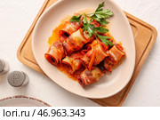 Тарелка с картофельным пюре, черносливом, запеченным в хрустящем беконе, подливным соусом и петрушкой на светлом столе, крупным планом. Стоковое фото, фотограф Pixel_shot / Фотобанк Лори