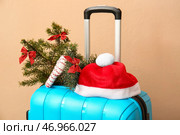 Чемодан, шляпа Санты и украшенная еловая ветка возле цветной стены, крупный план. Концепция рождественских каникул. Стоковое фото, фотограф Pixel_shot / Фотобанк Лори