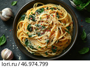 A plate of delicious pasta cooked in Italian style. The spaghetti is covered with a creamy sauce with garlic, spinach and grated Parmesan cheese. The dish is garnished with red chili flakes and finely chopped herbs, which adds brightness and piquancy. Fresh spinach leaves, garlic cloves and Parmesan crumbs are laid out around the plate against a dark background, creating a stylish gastronomic composition. The overall appearance of the pasta radiates coziness, aroma and richness of flavors. Стоковое AI-изображение, AI-художник Анна Кривицкая / Фотобанк Лори