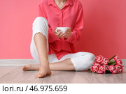 Босая женщина с чашкой чая и тюльпанами сидит у розовой стены. Стоковое фото, фотограф Pixel_shot / Фотобанк Лори