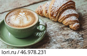 Green ceramic cup of frothy cappuccino coffee with croissants on rustic wood background. Hot latte with art milk foam and freshly-baked Brioche on cafe table. Breakfast or coffee break. Morning ritual. Стоковое AI-видео, аниматор Марина Демидюк / Фотобанк Лори