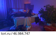 Stressed man lie on the bed at home while holding his head neon background. Стоковое фото, фотограф David Kashakhi / Фотобанк Лори
