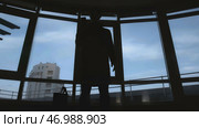 Dark shadow of man with bag pulls out phone on background of windows. Стоковое фото, фотограф David Kashakhi / Фотобанк Лори