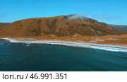 Mountain with rising smoke, blue sky above and wavy shore. Стоковое фото, фотограф David Kashakhi / Фотобанк Лори