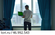 Back view of a young man in white t shirt working on laptop with green chroma key screen. Стоковое фото, фотограф David Kashakhi / Фотобанк Лори
