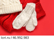 Пара белых вязанных варежек с теплой шапкой и шарфом на красном фоне. Стоковое фото, фотограф Pixel_shot / Фотобанк Лори