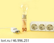 Деньги с лампочкой, вилкой и розеткой на желтом фоне. Концепция счетов за электроэнергию. Стоковое фото, фотограф Pixel_shot / Фотобанк Лори