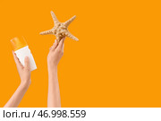 Женские руки с бутылкой крема для солнцезащиты и морской звездой на желтом фоне. Стоковое фото, фотограф Pixel_shot / Фотобанк Лори