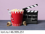Киношные щит и ведро с попкорном с хэллоуинским декором на деревянном столе на фоне лилового цвета. Стоковое фото, фотограф Pixel_shot / Фотобанк Лори