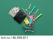 Бумажник, деньги и тележка для покупок с различными канцелярскими принадлежностями на зеленом фоне. Стоковое фото, фотограф Pixel_shot / Фотобанк Лори