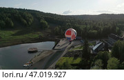 A stunning aerial view featuring a scenic lake alongside a colorful balloon attraction in nature. Стоковое фото, фотограф David Kashakhi / Фотобанк Лори