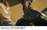 A male crew navigator stands on the hood of an SUV stuck in a muddy ditch and pulls the winch rope. Extreme racing. Стоковое фото, фотограф Воловодов Владимир / Фотобанк Лори